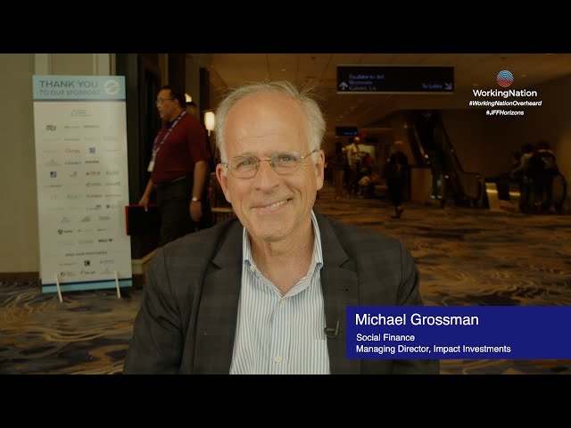 Video thumbnail. Michael Grossman sits on a chair in a busy room. He is wearing a suit and smiling.